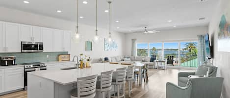 A modern kitchen with white cabinetry, a central island with bar stools, and a dining area with a view of the outdoors.