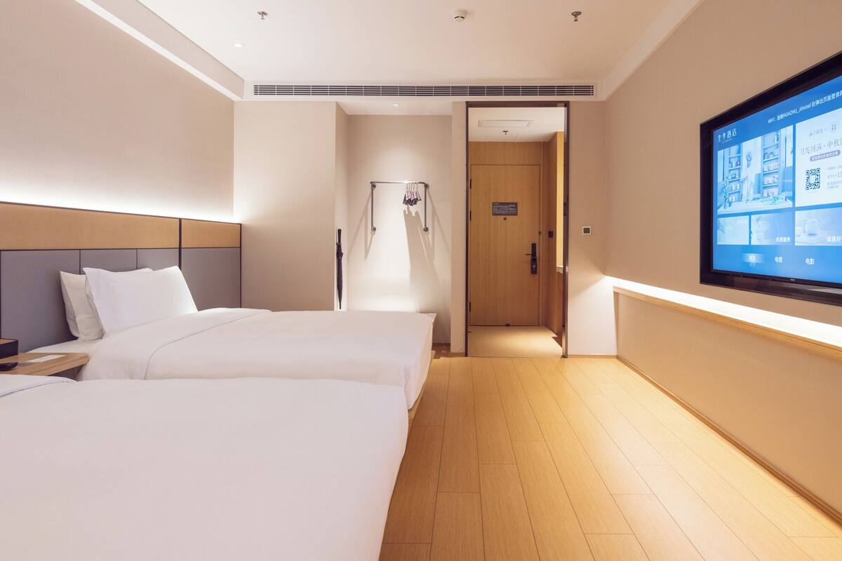 A hotel room with two beds, a TV on the wall, and a wooden floor.