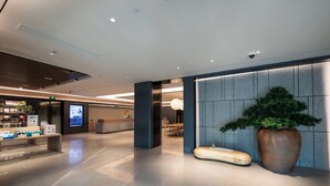 A modern hotel lobby with a reception desk, seating area, and a large potted plant. - Ji Hotel Shanghai Pudong Airport Free Trade Zone (Shanghai)