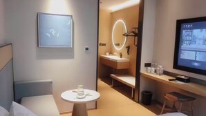 A modern hotel room with a bed, a small round table, a TV, a mirror, and a bathroom visible through an open door. - Ji Hotel Shanghai Pudong Airport Free Trade Zone (Shanghai)
