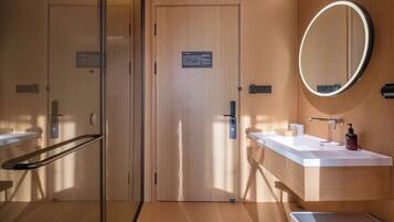 Un baño moderno con paredes de madera, cabina de ducha con vidrio y un espejo redondo.