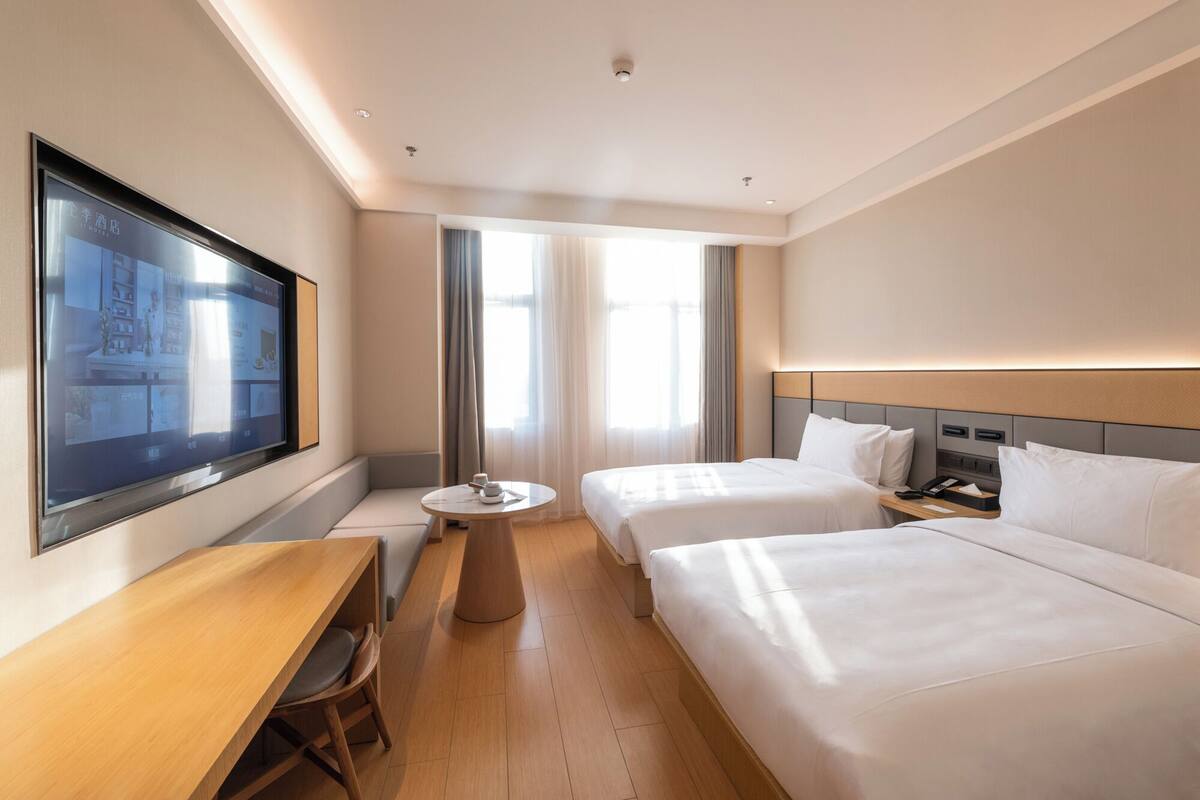 A hotel room with two beds, a desk, a chair, a small round table, and a TV mounted on the wall.
