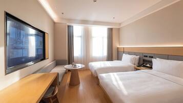 A hotel room with two beds, a desk, a chair, a small round table, and a TV mounted on the wall.