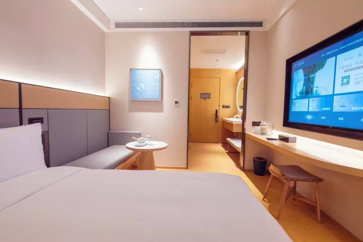 A hotel room with a bed, a small table, a TV, and a desk.