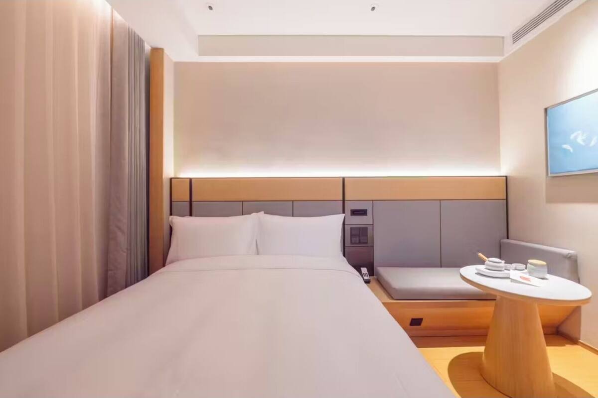 A hotel room with a large bed, a bedside table, a small seating area, and a wall-mounted TV.