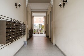 A corridor with mailboxes, a trash bin, and a view of buildings in the distance.