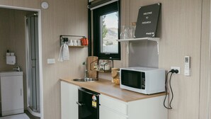Cocina compacta con microondas, lavabo y un refrigerador pequeño. Hay una ventana con vistas al exterior, y un cartel de bienvenida encima de la ventana.