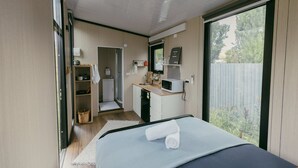 Un dormitorio moderno con cama, una kitchenette pequeña, un baño y una puerta corrediza de vidrio al exterior.