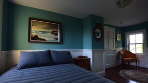 A bedroom with a bed, a painting, a chair, and a window.