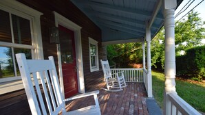 A covered porch with white rocking chairs and a red door.
