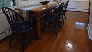 A dining area with a wooden table and chairs, a painting on the wall, and a window with blinds.