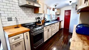 A kitchen with white tiled backsplash, wooden countertops, a stove, and a red door.