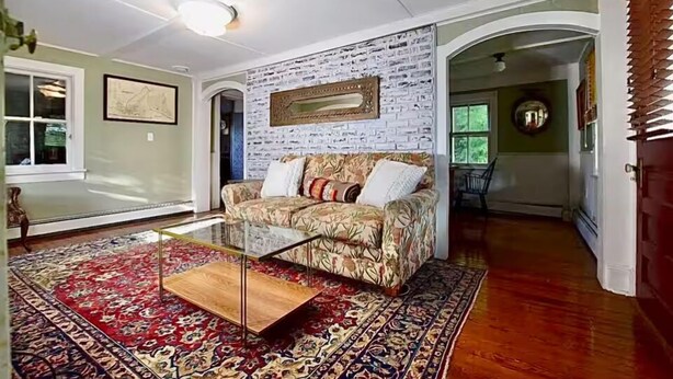 A living room with a patterned sofa, a glass coffee table, and a red and blue patterned rug.