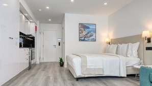 Een moderne hotelkamer met een groot bed, een kitchenette en een schilderij van een kustlandschap.