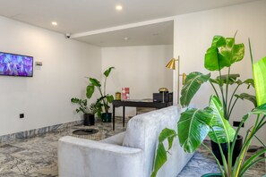 Ein stilvolles Wohnzimmer mit Marmorboden, einem grauen Sofa, einem Couchtisch und mehreren Blumentöpfen.