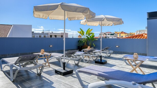 A rooftop lounge area with sun loungers, umbrellas, and a potted plant.