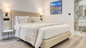 A modern hotel room with a large bed, two bedside lamps, a small table with a glass, and a painting of a coastal scene.