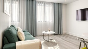 A modern living room with a green sofa, a small round table, and a large window with sheer curtains.