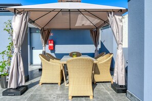 Eine Terrassengruppe mit Korbmöbeln, einem Tisch und einem großen Sonnenschirm.