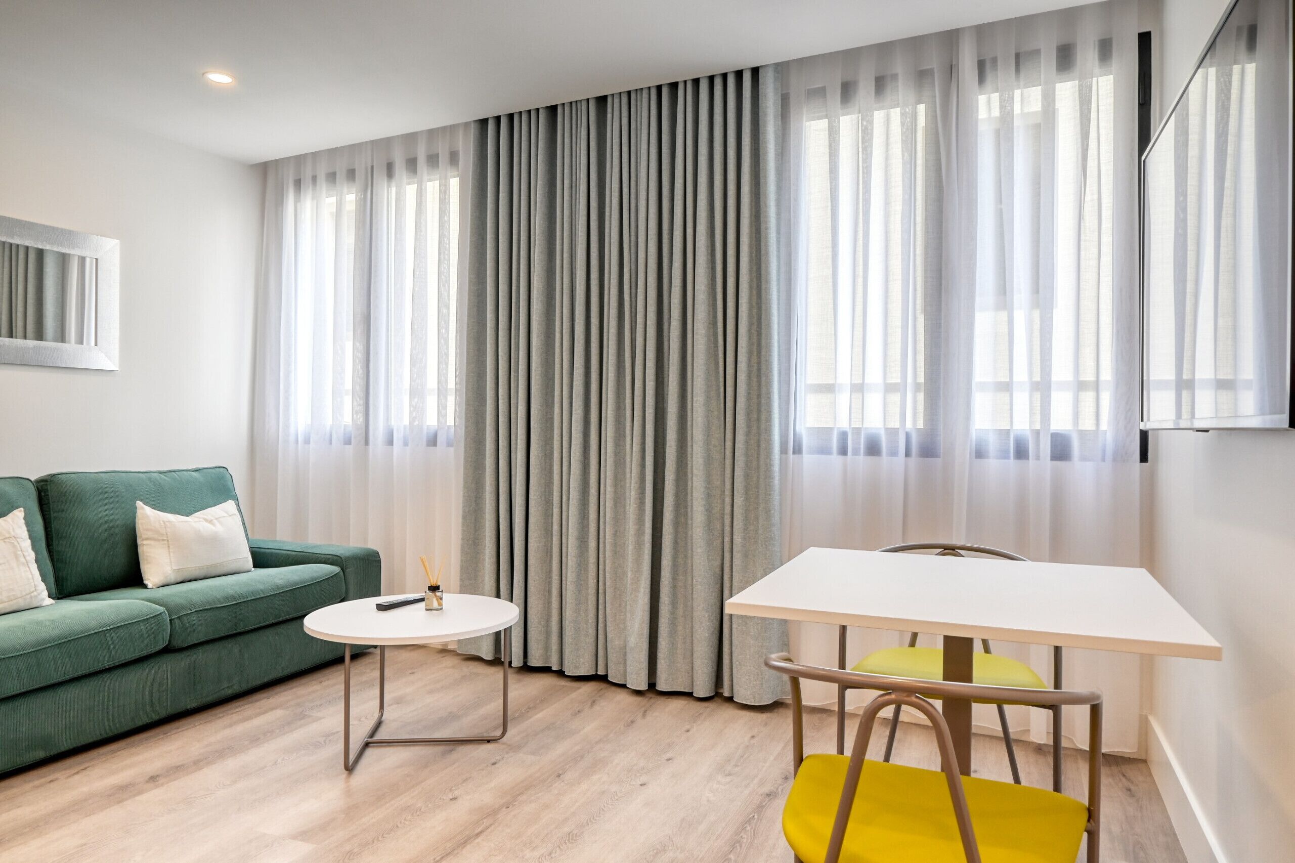 Ein modernes Wohnzimmer mit einem grünen Sofa, einem runden weißen Tisch und einem gelben Sessel.