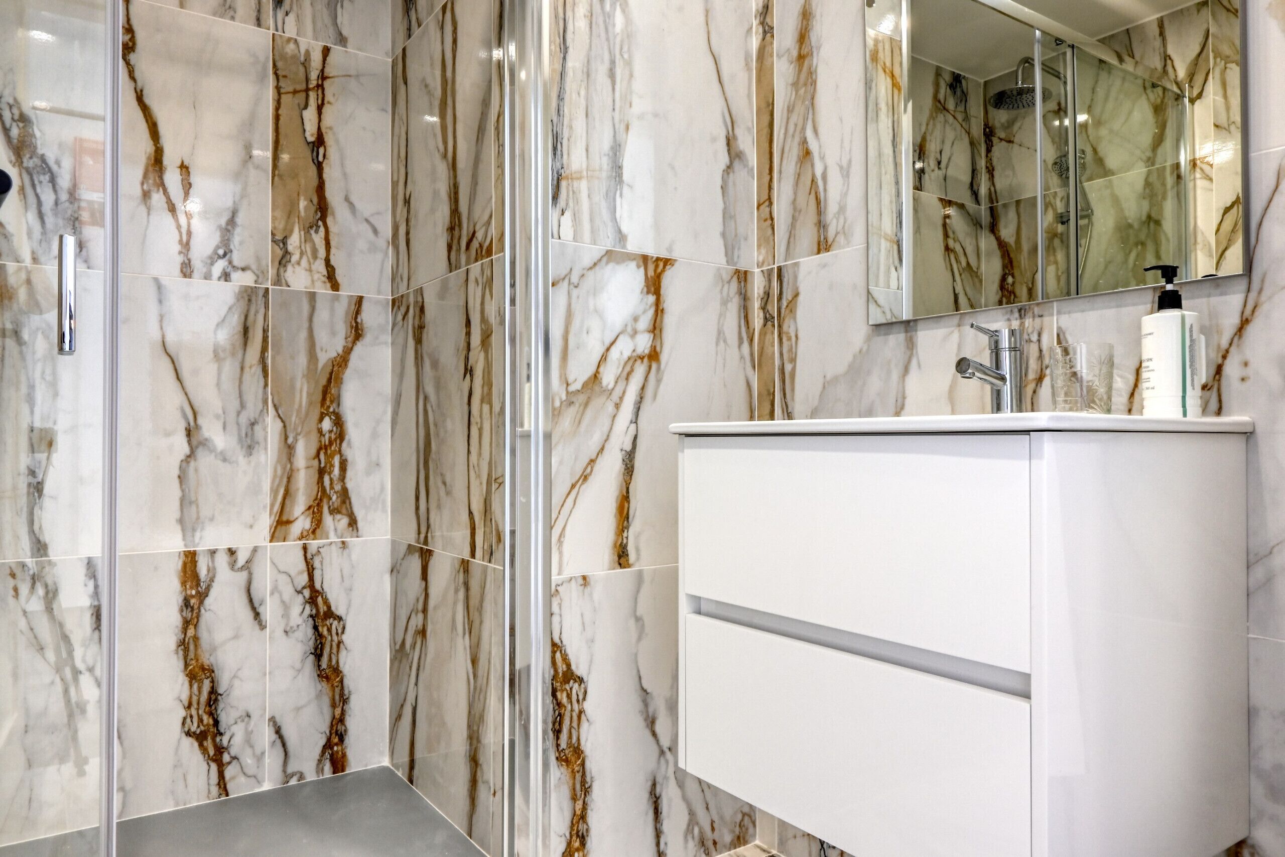 Un baño moderno con paredes de mármol y un tocador blanco.