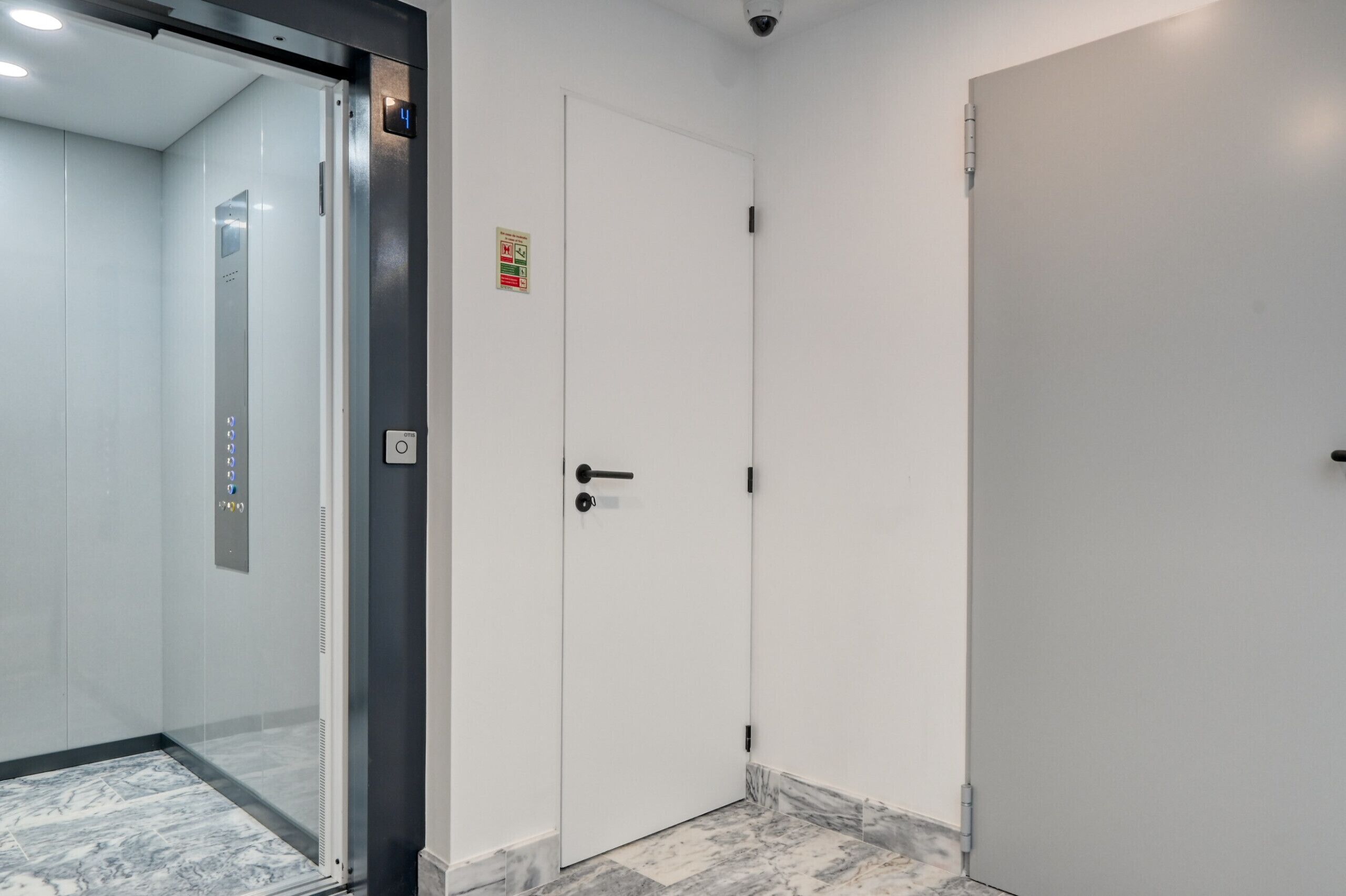 A modern elevator with a control panel, a white door with a safety sign, and a marble-tiled floor.