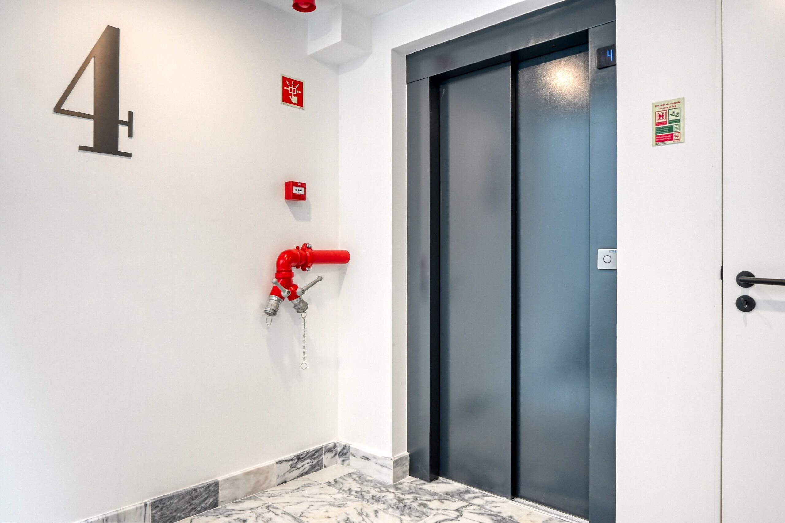 Ein moderner Aufzug mit digitaler Anzeige, einem Feuerlöscher und einem Feueralarm an der Wand.