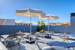 A rooftop lounge area with sun loungers, umbrellas, and a potted plant.