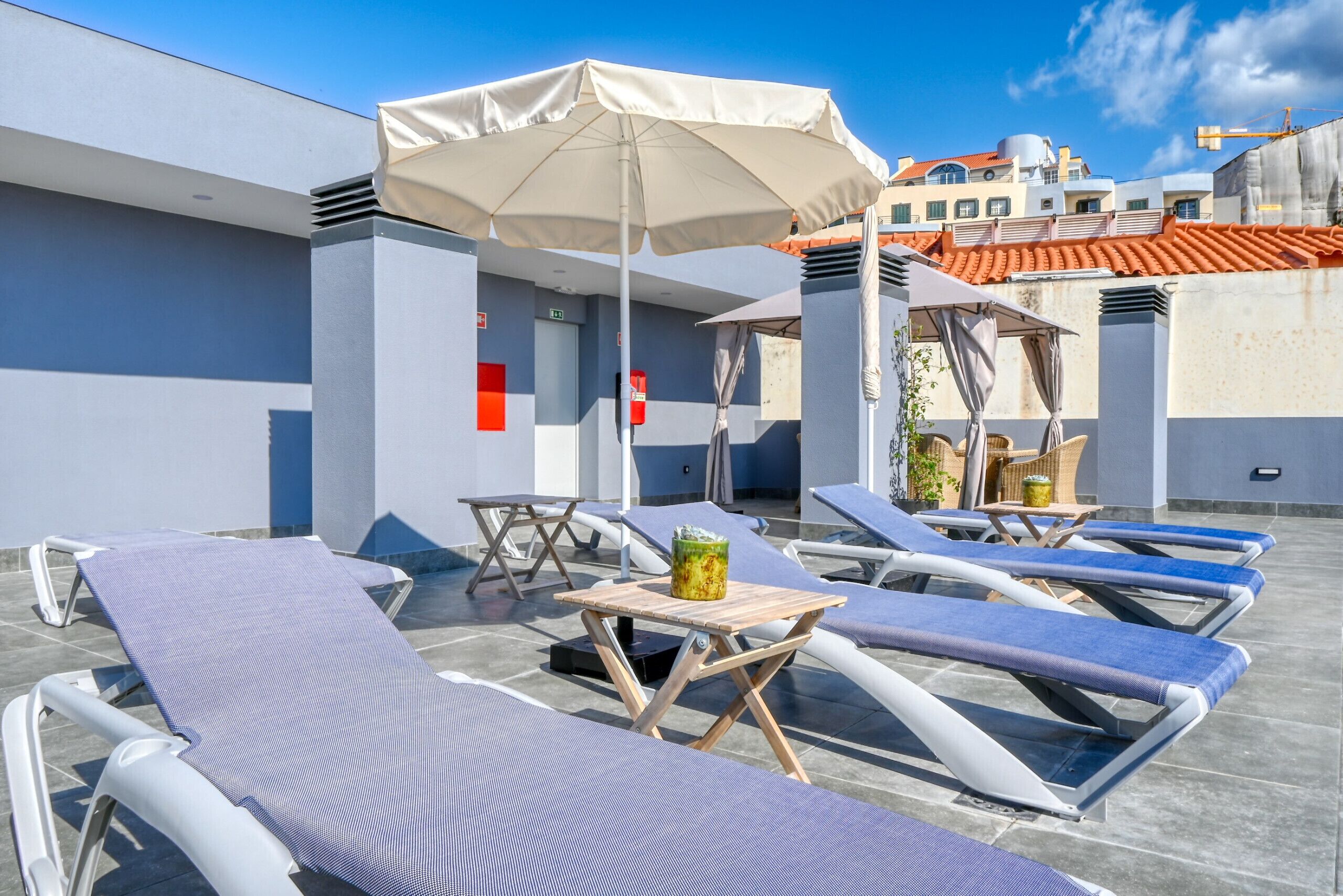 A rooftop lounge area with sun loungers, a table with a drink, and umbrellas.