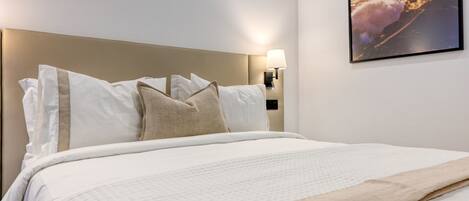 A hotel room with a large bed, a headboard, a wall-mounted lamp, and a framed picture on the wall.