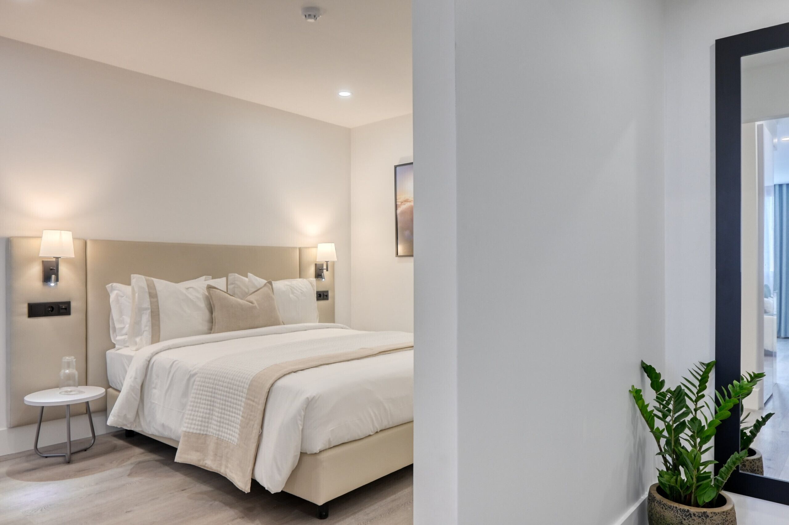 Un dormitorio moderno con una cama grande, lámparas de noche, una mesita redonda y una planta en maceta.