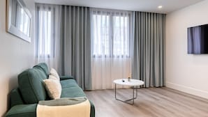 En moderne stue med en grøn sofa, et rundt bord og et stort vindue med grå gardiner.
