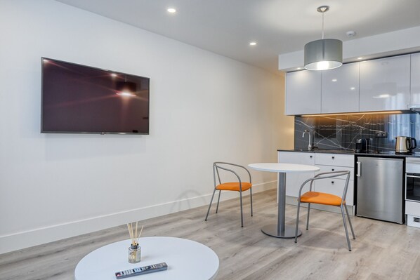 A modern kitchen with a flat-screen TV, two chairs, a small table, and a coffee machine.