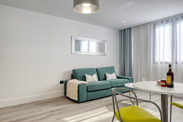 Ein modernes Wohnzimmer mit einem grünen Sofa, einem runden weißen Tisch und einem Spiegel an der Wand.