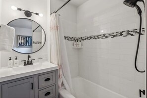 A bathroom with a white vanity, a round mirror, a shower with a black hose, and a tiled shower area.