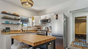 A modern kitchen with white cabinets, stainless steel appliances, a wooden dining table, and a fur-covered stool. - Daly Cottage | Walk to Main | Monthly Rentals Ava. (Park City)