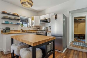 A modern kitchen with white cabinets, stainless steel appliances, a wooden dining table, and a fur-covered stool.