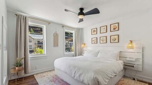 A bedroom with a bed, a ceiling fan, a window with curtains, a wall-mounted lamp, and framed pictures. - Daly Cottage | Walk to Main | Monthly Rentals Ava. (Park City)