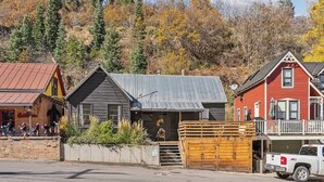 A rustic building with a metal roof, a wooden porch, and a garage. - Daly Cottage | Walk to Main | Monthly Rentals Ava. (Park City)