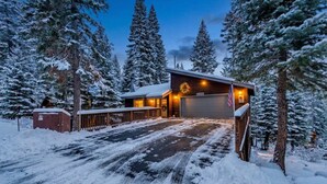Un paysage enneigé avec une cabane dotée d’un garage et d’une guirlande illuminée accrochée à la porte.