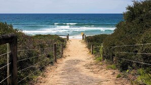 Un camí de fusta que condueix a la platja, envoltat de vegetació i amb una vista despejada de l'oceà.