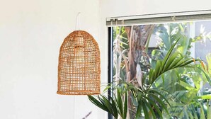 Una habitació amb una finestra gran, una taula de vimetera amb un ram de flors blanques, i una làmpada penjant de vimetera.
