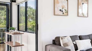 Un saló modern amb un sofà gris, una taula rodona petita i una taula de centre blanca. Hi ha dues obres d'art emmarcades a la paret i una porta corredissa de vidre que dona a un balcó.