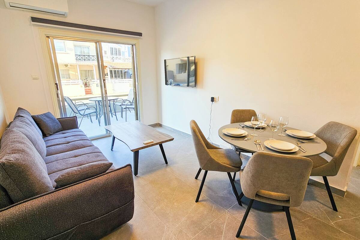 Un coin repas avec une table ronde pour quatre personnes, un canapé et un téléviseur fixé au mur.