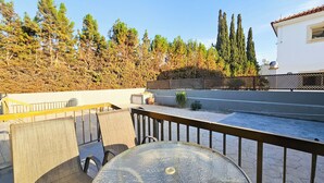 Une terrasse sur le toit, avec une table et des chaises, donnant sur une rue et bordée d’une rangée d’arbres.