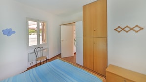 Een slaapkamer met een bed, een kledingkast, een stoel en een raam.
