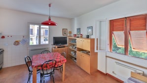 Een kleine keuken met een eettafel, stoelen, een televisie en een raam met luiken.