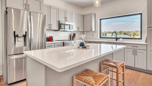Une cuisine moderne dotée d’appareils électroménagers en acier inoxydable, d’un grand îlot central et offrant une vue par la fenêtre.