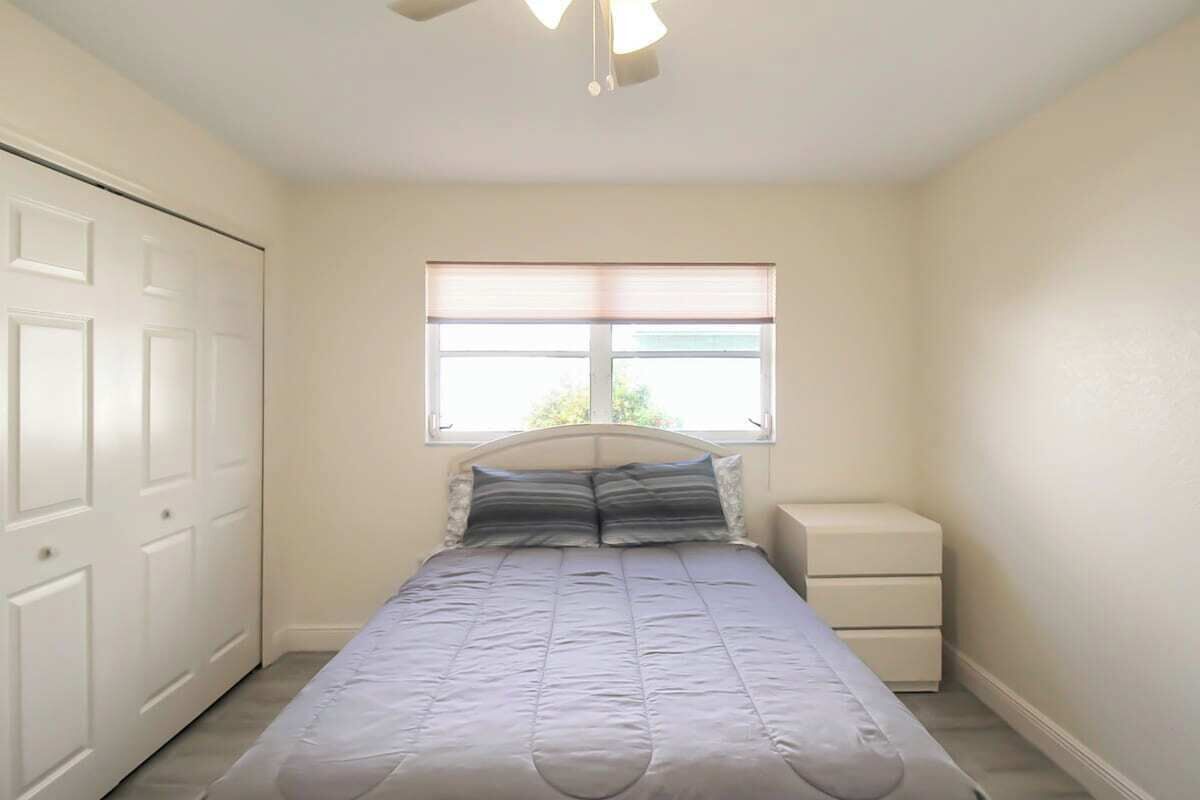 A bedroom with a bed, a nightstand, a window, and a door.