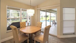 A dining area with a round table and four chairs, large windows with blinds, a chandelier, and a view of a backyard with a pool. - Stunning 3/2 pool home in the heart of Punta Gorda - Pelican Poolside (Punta Gorda)